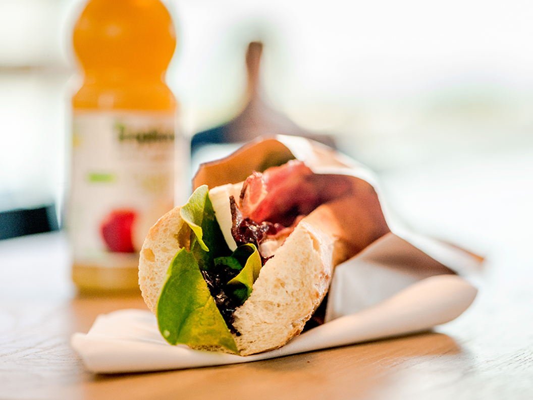 Nylaget sandwich med salat, bacon og ost på et trebord, ledsaget av en flaske appelsinjuice i bakgrunnen