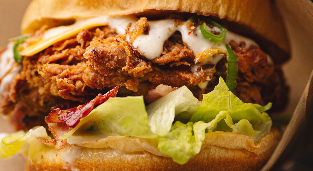Nærbilde av en sprø, fritert kyllingsandwich med salat, bacon og kremet saus på en ristet hamburgerbrød