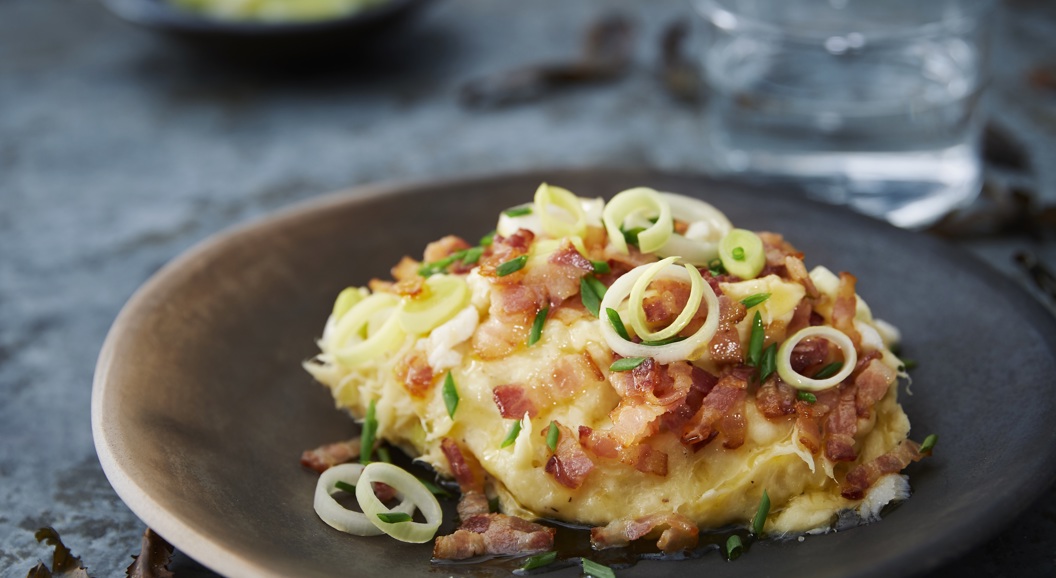 Kremet potetgrateng toppet med sprø bacon og fersk vårløk, servert på en rustikk keramikkfat