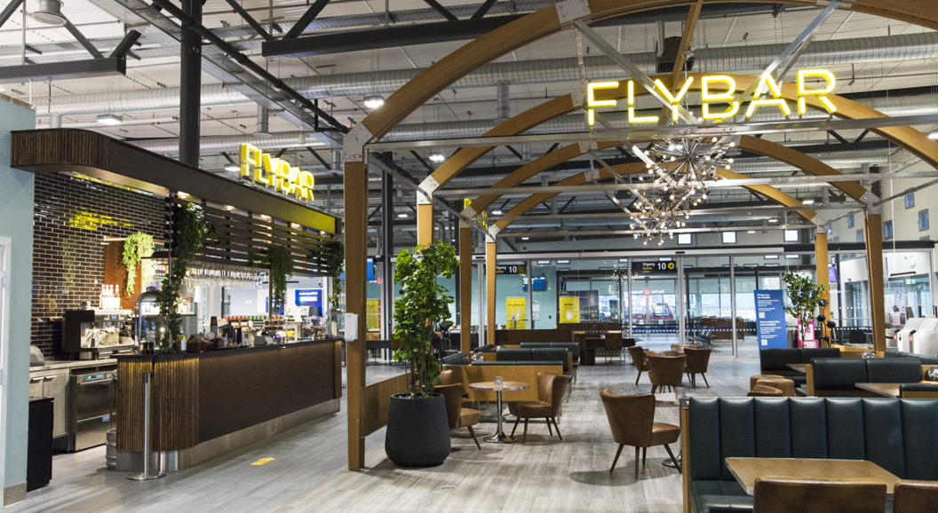 Moderne flyplassbar med stilige sitteplasser og opplyst "FlyBar"-skilt, med buede trebjelker og moderne innredning