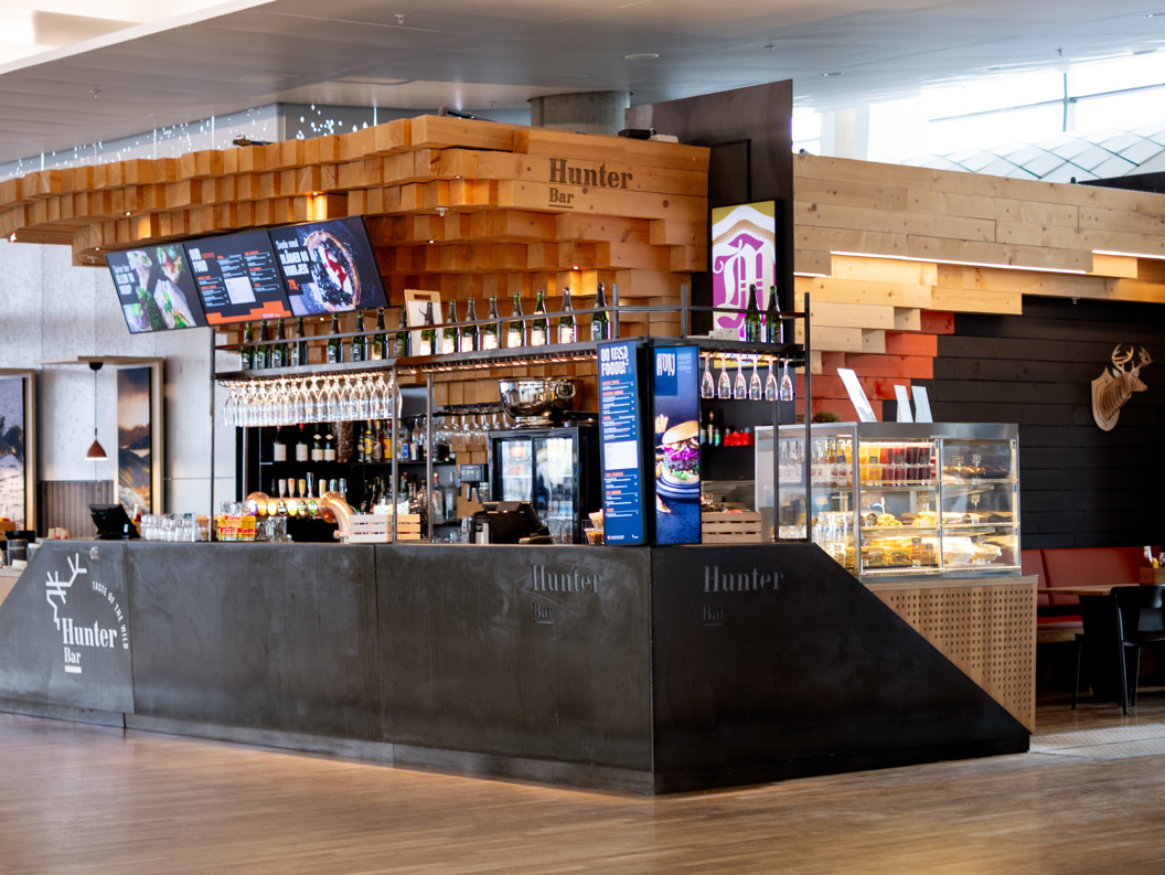 Moderne kafe med tresøyler og glasmonter, serverer drikke og snacks i ein flyplasslounge
