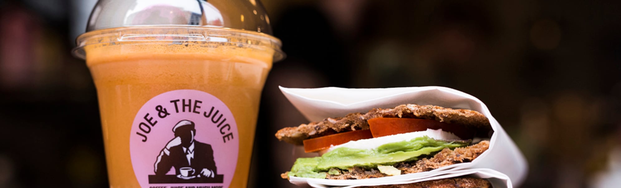 Kaldpressa juice frå "Joe & The Juice" ved sidan av ein sunn sandwich med avokado, tomat og mozzarella i brød servert på kafé