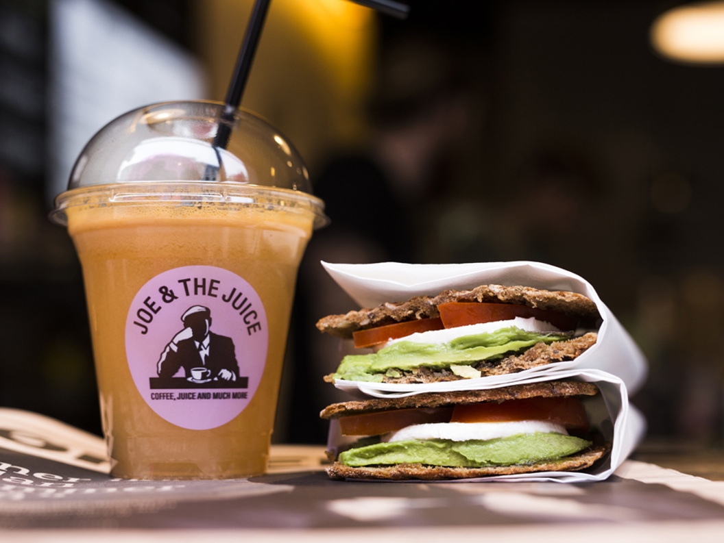 Kaldpressa juice frå "Joe & The Juice" ved sidan av ein sunn sandwich med avokado, tomat og mozzarella i brød servert på kafé