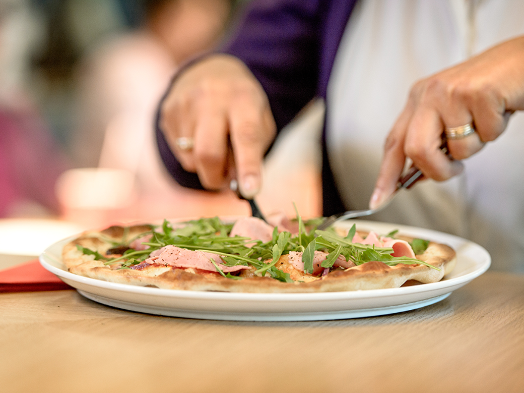 Person et pizza med ruccola og skinke med kniv og gaffel