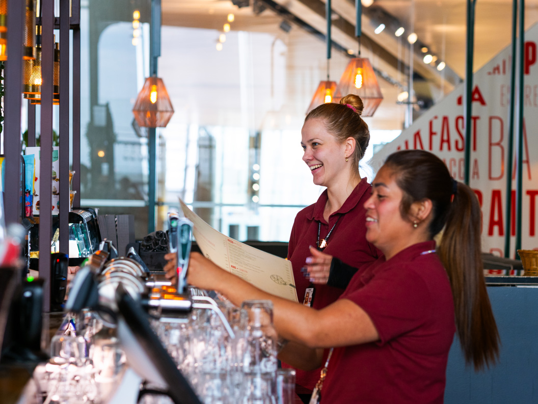 To servitørar arbeider saman bak ein bar i ein restaurant, omgitt av glas og moderne belysning