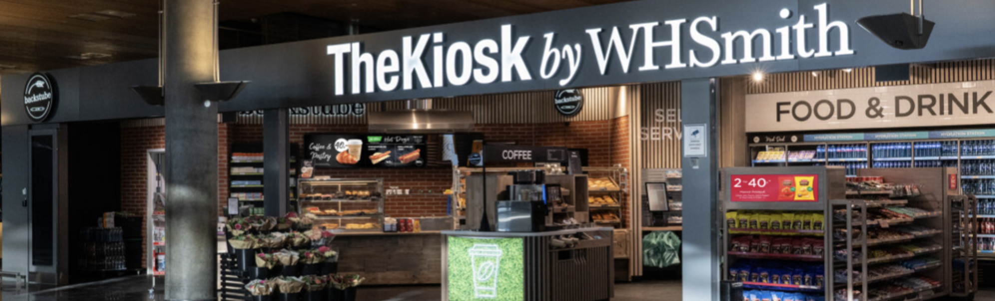 Matvarekiosk The Kiosk by WHSmith på ein flyplass, med hyller fulle av snacks, drikke og daglegvarer