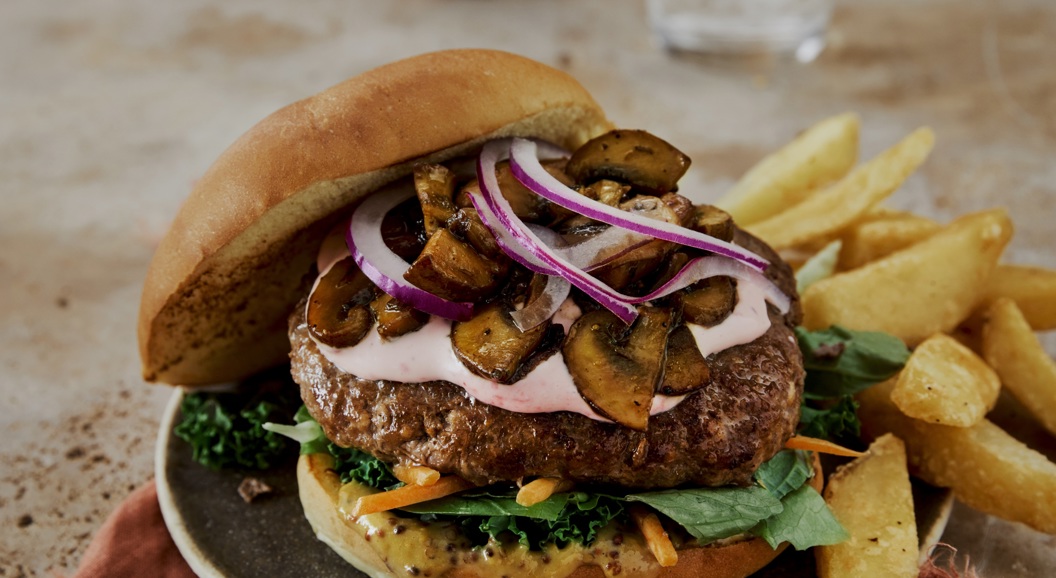 Saftig burger med sopp, rødløk og grønt på en tallerken, servert med grove pommes frites