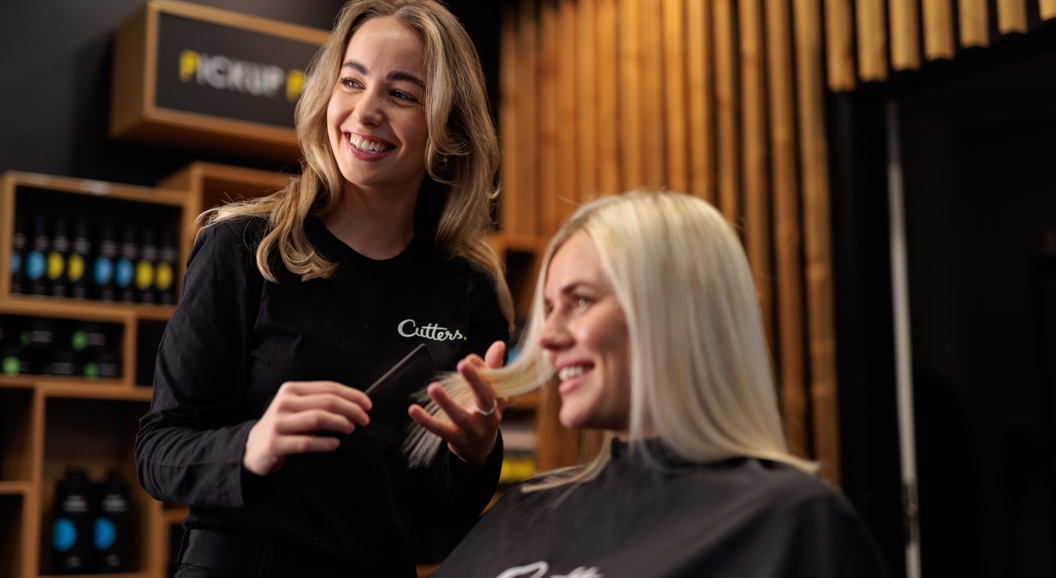 Frisør smiler medan ho friserer ein kunde med langt blondt hår i ein moderne frisørsalong