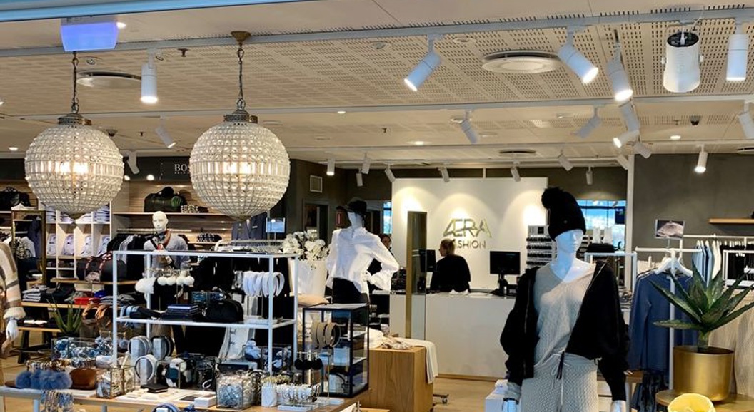 Motebutikk med namnet ÆRA, viste eit elegant interiør med klede, tilbehør og dekor på utstilling. Moderne lysdesign og velordna butikkmiljø