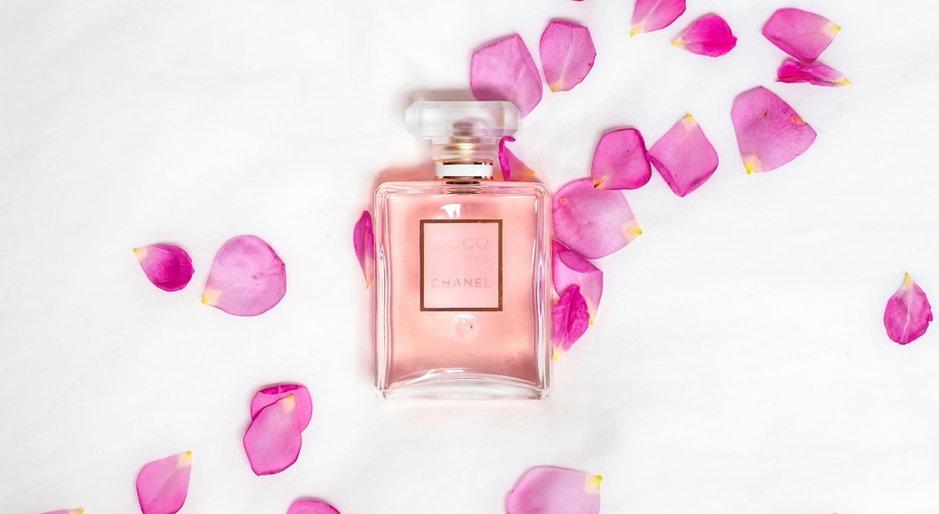 Rosa parfymeflaske omgitt av rosa roseblader på en hvit bakgrunn, som skaper en elegant og feminin estetikk