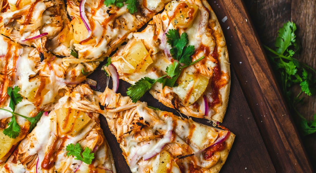Barbecue kyllingpizza med ananas, rødløk og koriander på et skjærebrett av tre
