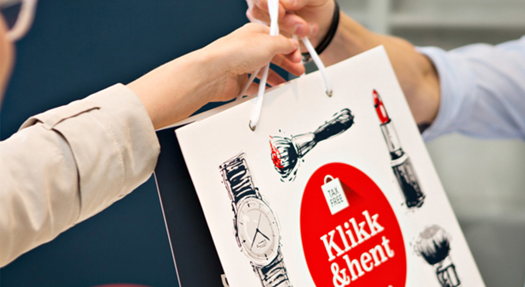Close-up of hands exchanging a shopping bag with illustrations of a watch, lipstick, and a brush, featuring the text "Klikk & hent" and a tax-free tag, symbolizing convenient, tax-free shopping