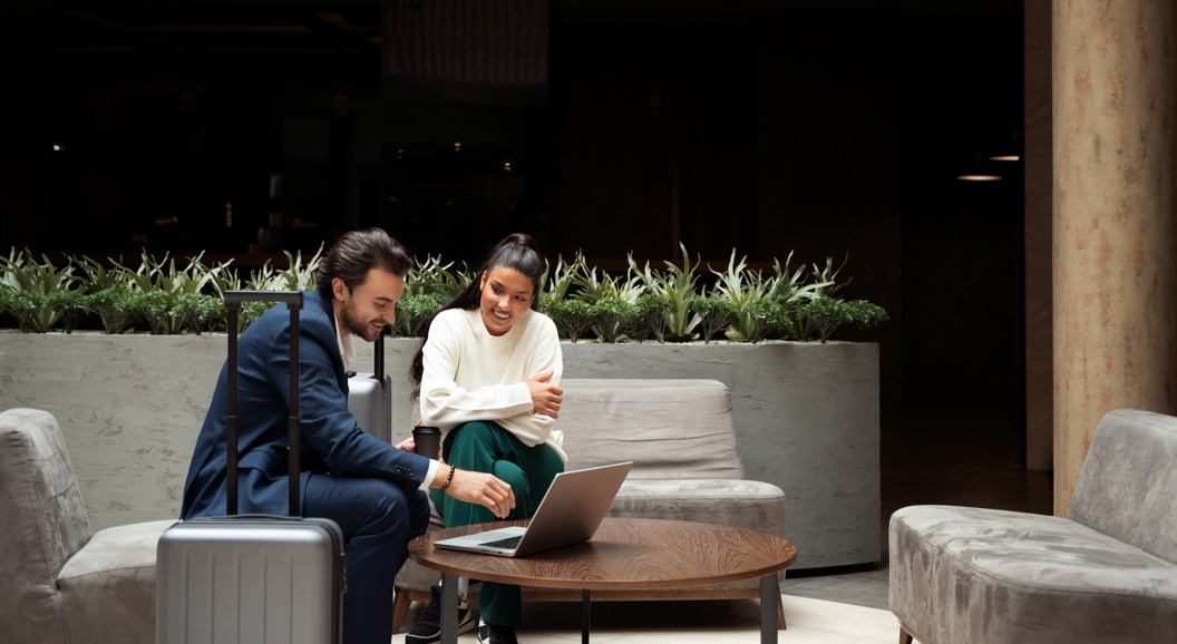 Business professionals discussing work on a laptop in a modern lounge area with a suitcase nearby