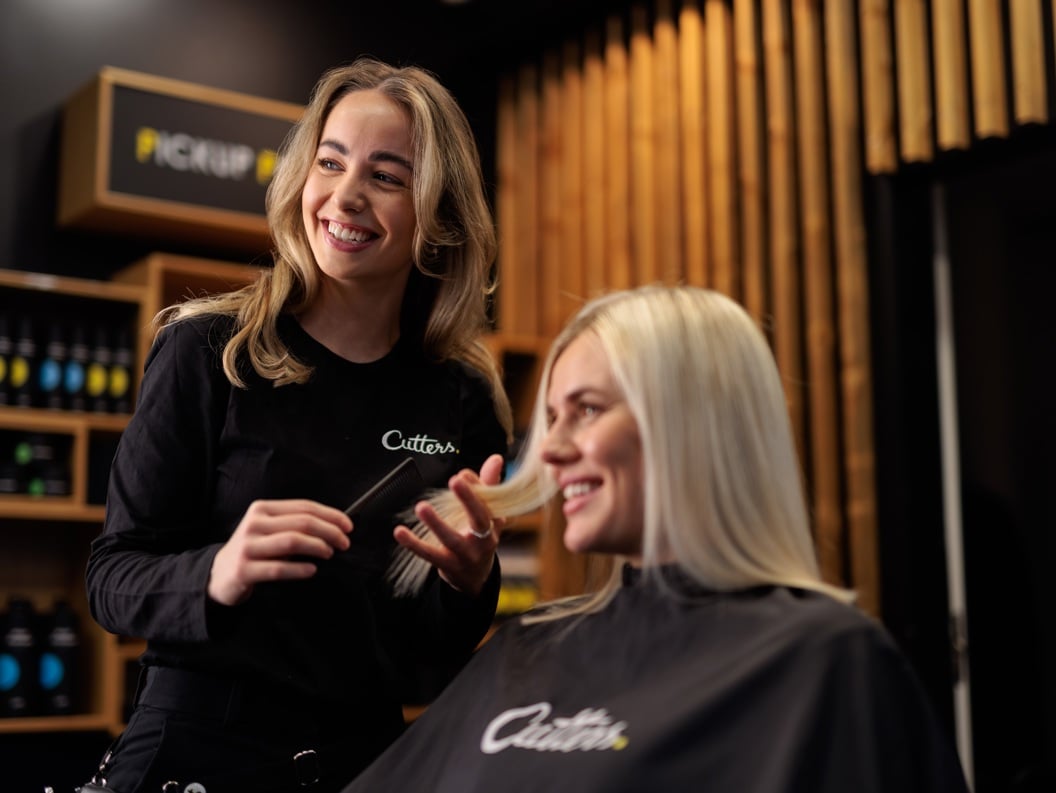 Smiling hairstylist with long hair serving a blonde client in a modern salon