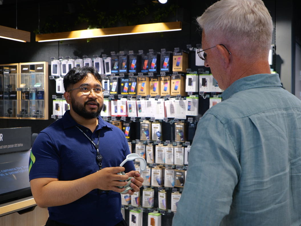 Store employee assisting a customer with earphones in a modern electronics shop, surrounded by phone accessories