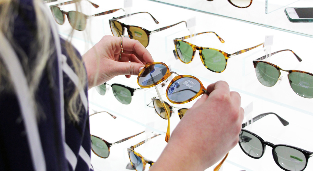 Person browsing a display of designer sunglasses in a store, examining tortoiseshell frames under bright lighting