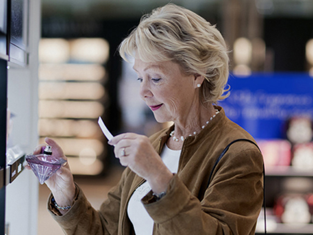 Senior woman testing perfume in a retail store, examining fragrance options