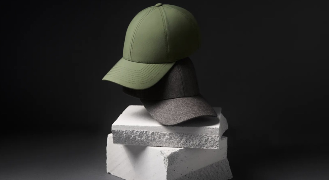 Two stylish caps, one green and one gray, are placed on stacked white concrete blocks with a dark background