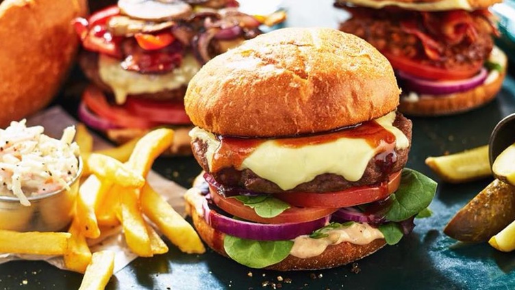 Gourmet cheeseburger med sprøstekt løk, salat og tomater på en ristet bolle, servert med en side av gyldne pommes frites i en metallkopp