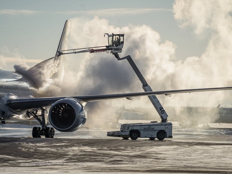 Et passasjerfly blir av-iset på en flyplass, med damp som stiger opp i kulden. En de-isebil er i aksjon under klar himmel.