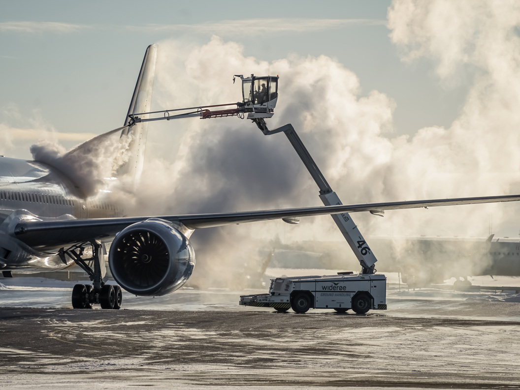 Fly som gjennomgår avriming på flyplassen ved bruk av spesialutstyr, med damp i vintermiljøet