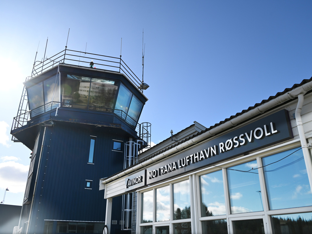 Vinterlandskap ved Mo i Rana flyplass med kontrolltårn, snødekte fjell i bakgrunnen, og oversvømt rullebane.