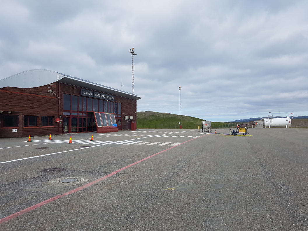 Båtsfjord lufthamn terminalbygning på ein overskya dag, med rullebane og grasdekte åsar i bakgrunnen.