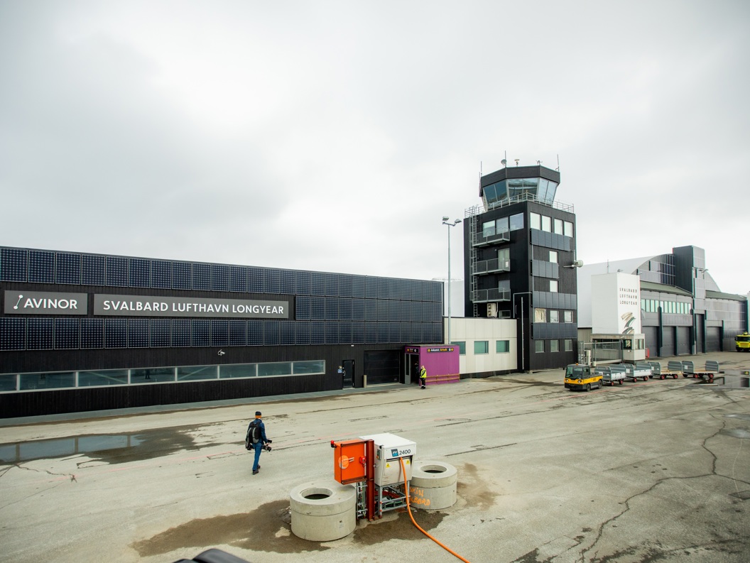 Svalbard lufthavn i Longyearbyen, med terminalbygningen og kontrolltårnet i forgrunnen, under overskyet vær.