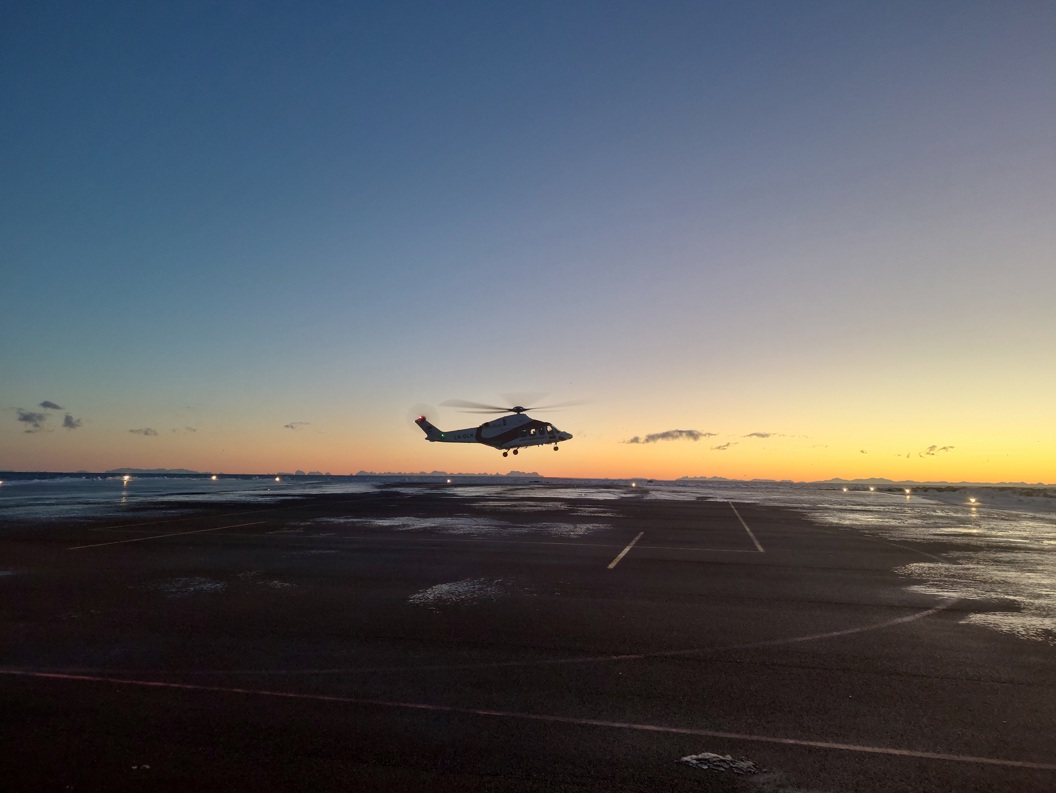 Helikopter lander på flyplass ved solnedgang med vakker himmelfarge i bakgrunnen.