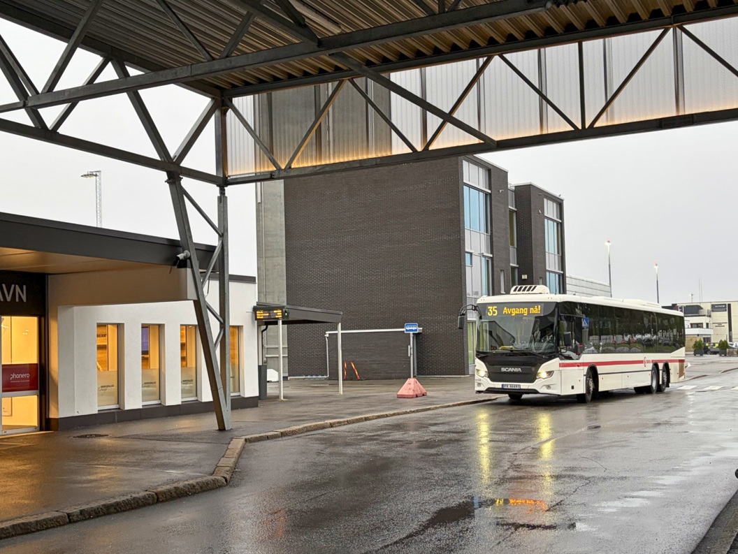 Buss 35 på våt holdeplass ved moderne terminalbygning i regnvær