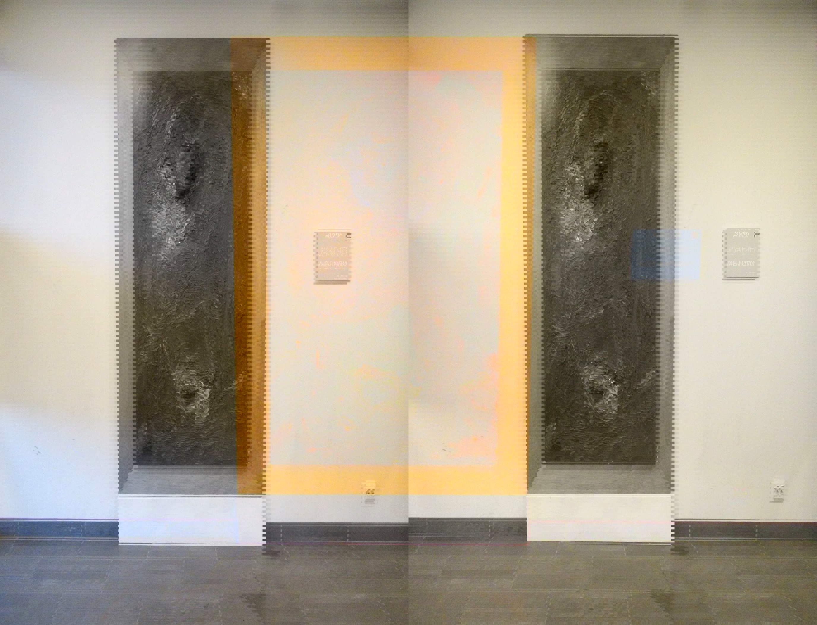 Vegghengt kunstverk i tre og metall, innrammet i en lystonet treramme, plassert i en lys gang