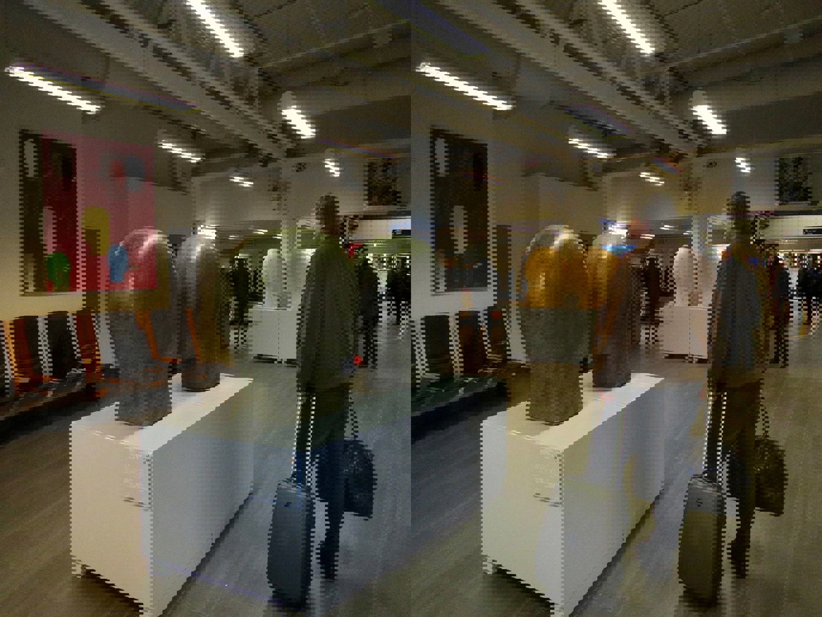 Kunstutstilling på flyplass; skulpturer av hoder på sokler, passasjer med koffert går forbi