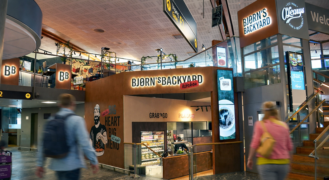 Bjørns Bakgårdskjøkken restaurantinngang i et kjøpesenter, med et veggmaleri av en skjeggete mann som holder mat, med slagordene "Stor Hjerte Stor Meny" og "Grab 'N Go, Pick Up