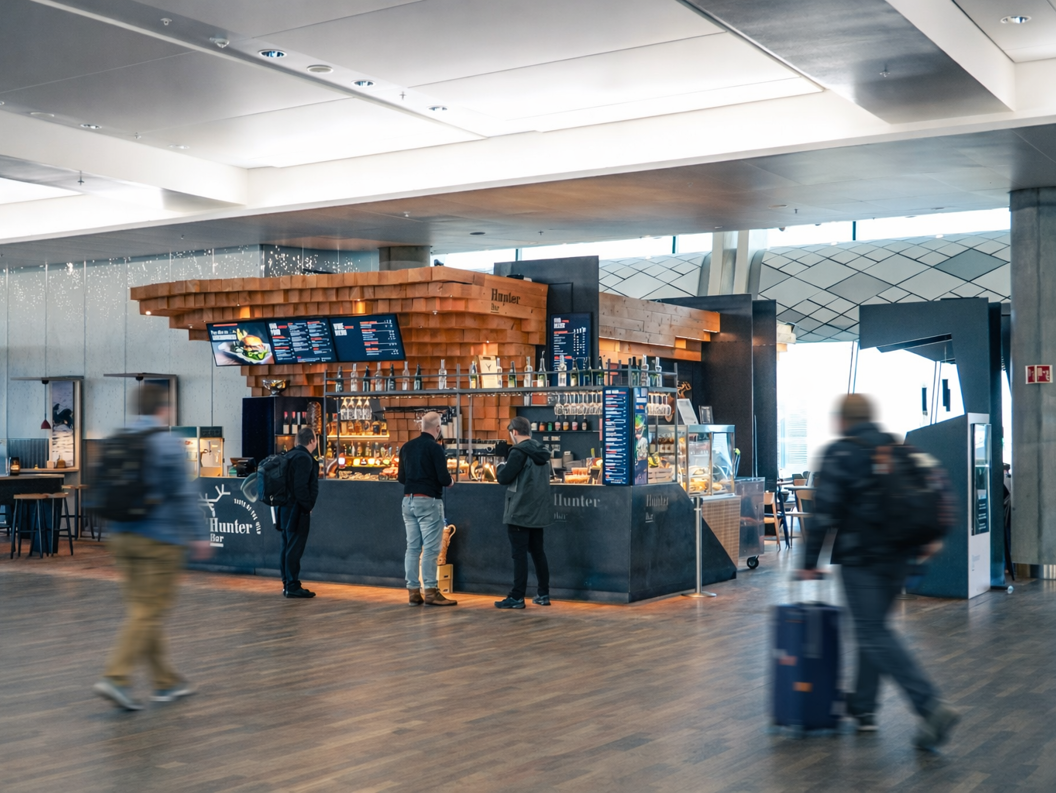 Moderne barinteriør med treinnslag og slankt design på Hunter Bar, som viser en digital meny, hengende glass og en utstillingsmonter med matvarer