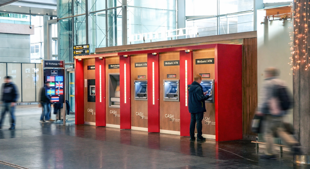 A person using an ATM at an airport, featuring various currency options and an exchange rate display