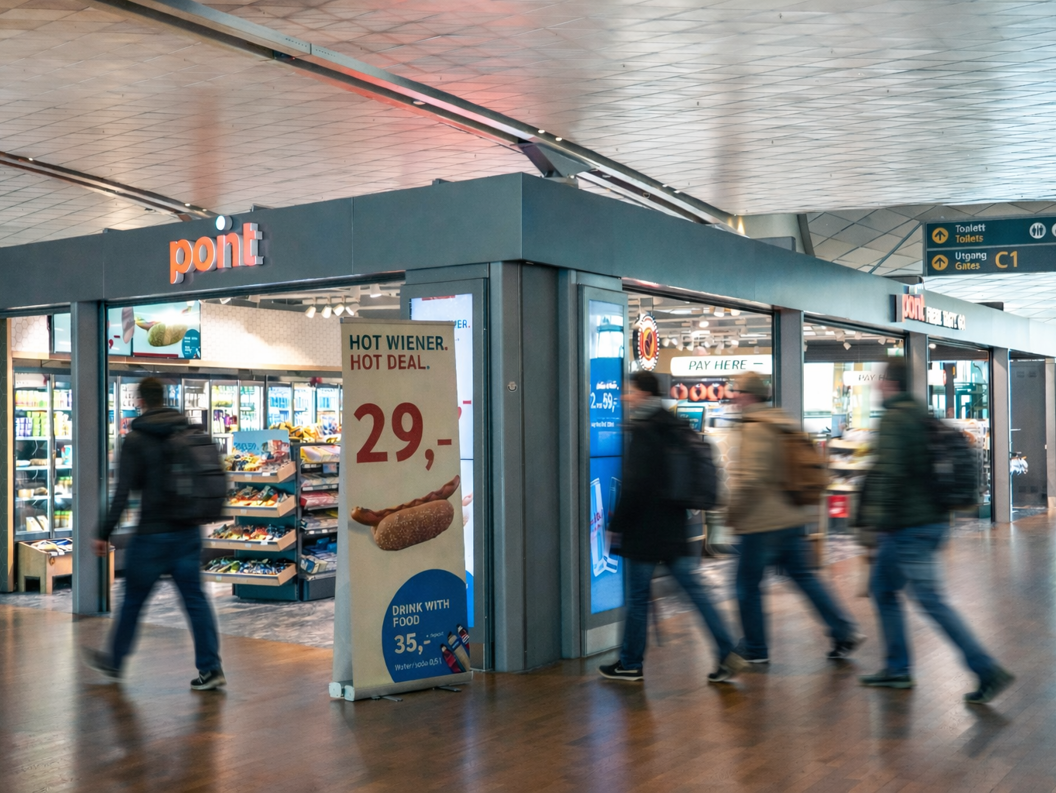 Smiling cashier in a blue uniform at a convenience store counter, with a promotional sign in the background