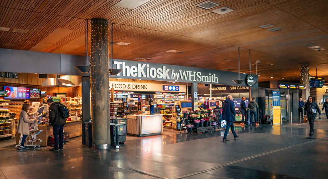 Moderne WHSmith-kiosk på en flyplass som tilbyr bekvemmelighetsvarer, snacks og drikkevarer under vibrerende belysning
