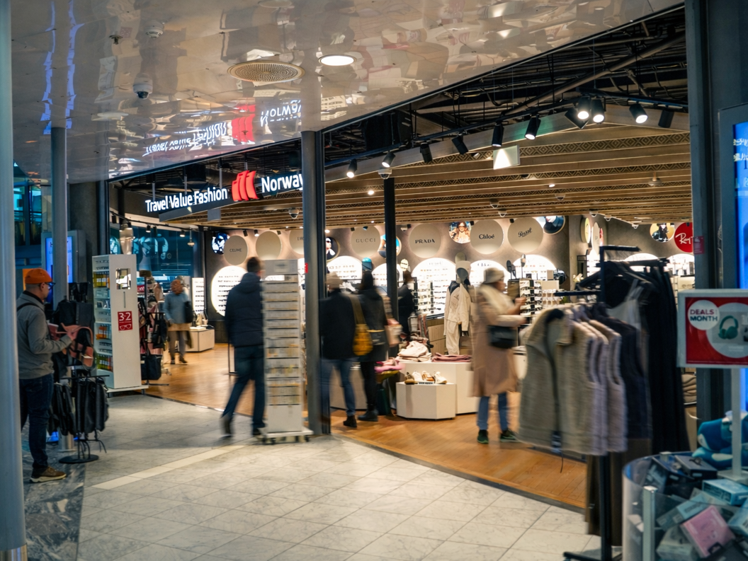 Kvinne som handler solbriller i en moderne butikk, iført en svart skinnjakke og smiler mens hun prøver et par solbriller