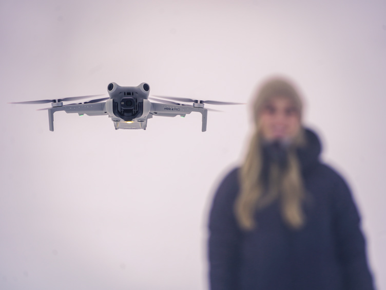 Gray drone flying in the air with a young woman in the background
